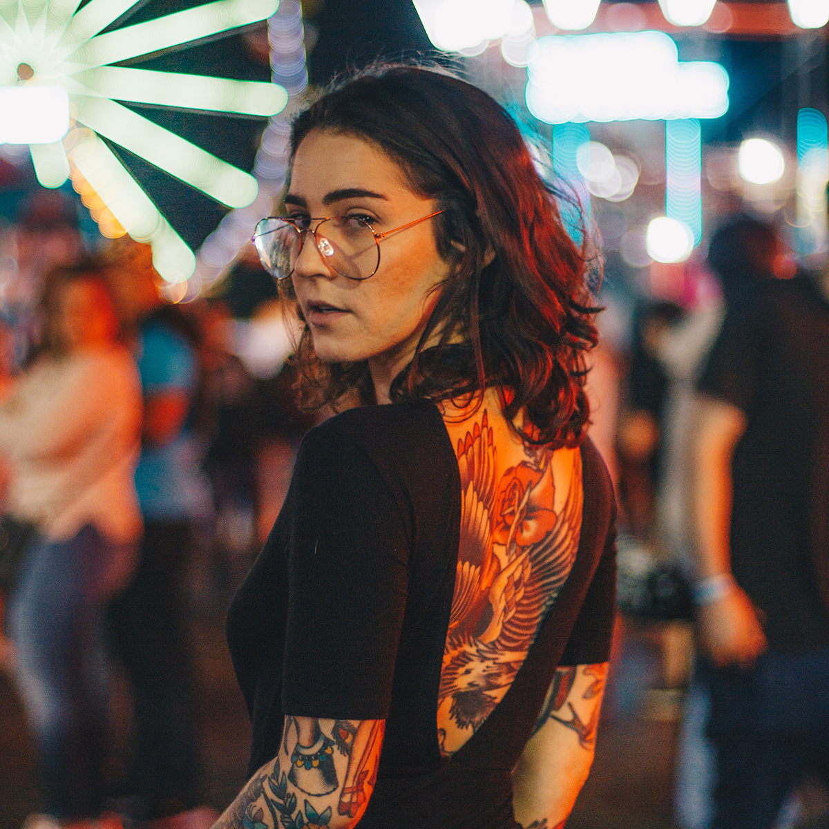 Une femme tatouée de dos regarde la caméra par dessus son épaule